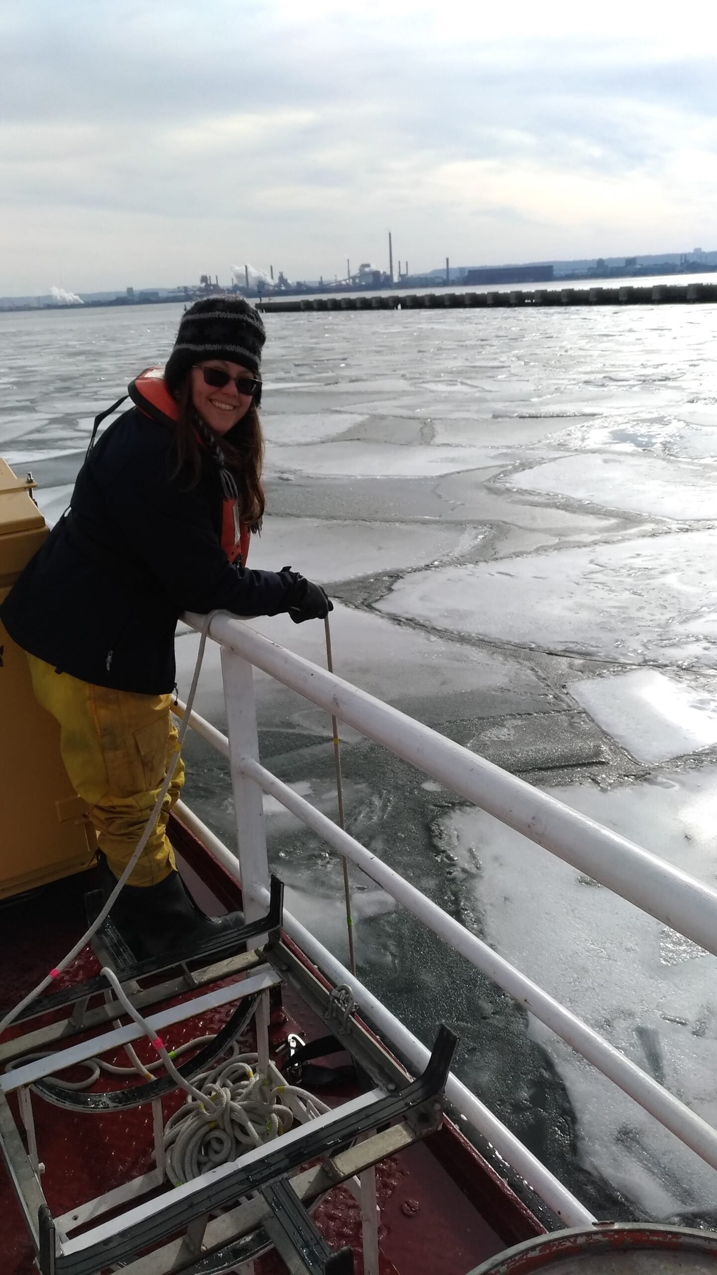 Biologist sampling with a rope off a ship's rail into water covered with ice floes.