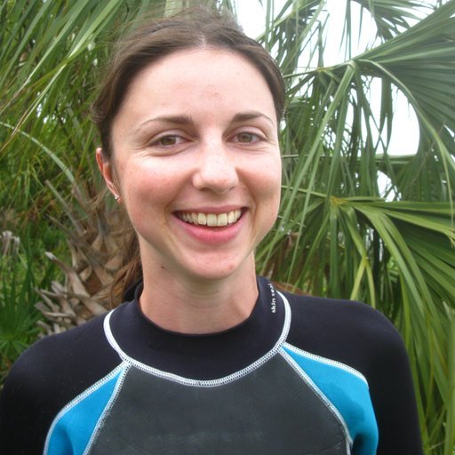 Colette standing in front of palm trees wearing a dive suit.