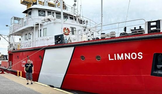 Person in a Canada shirt standing in front of a red and white coast guard ship with LIMNOS on the side.