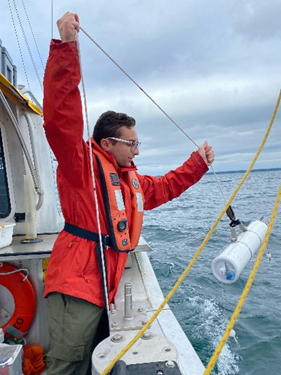 Technician field sampling deploying Van Dorn water sampler from side of boat.