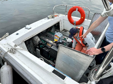 A worker checking the engine compartment of a small vessel.